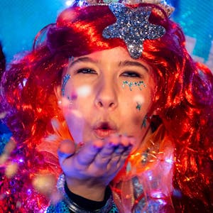 Eine Karnevalistin mit einer roten Perücke und einem silbernen Stern im Haar wirft den Jecken beim Lichterzug in Eiserfey eine Kusshand zu.