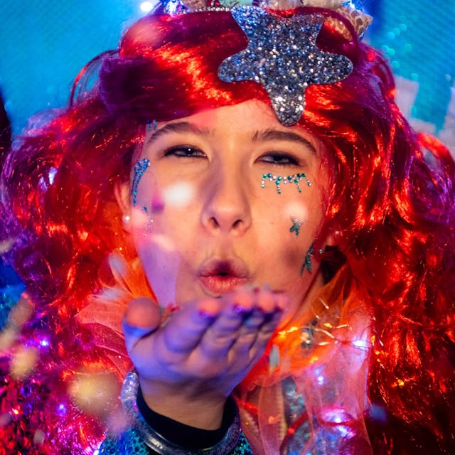 Eine Karnevalistin mit einer roten Perücke und einem silbernen Stern im Haar wirft den Jecken beim Lichterzug in Eiserfey eine Kusshand zu.