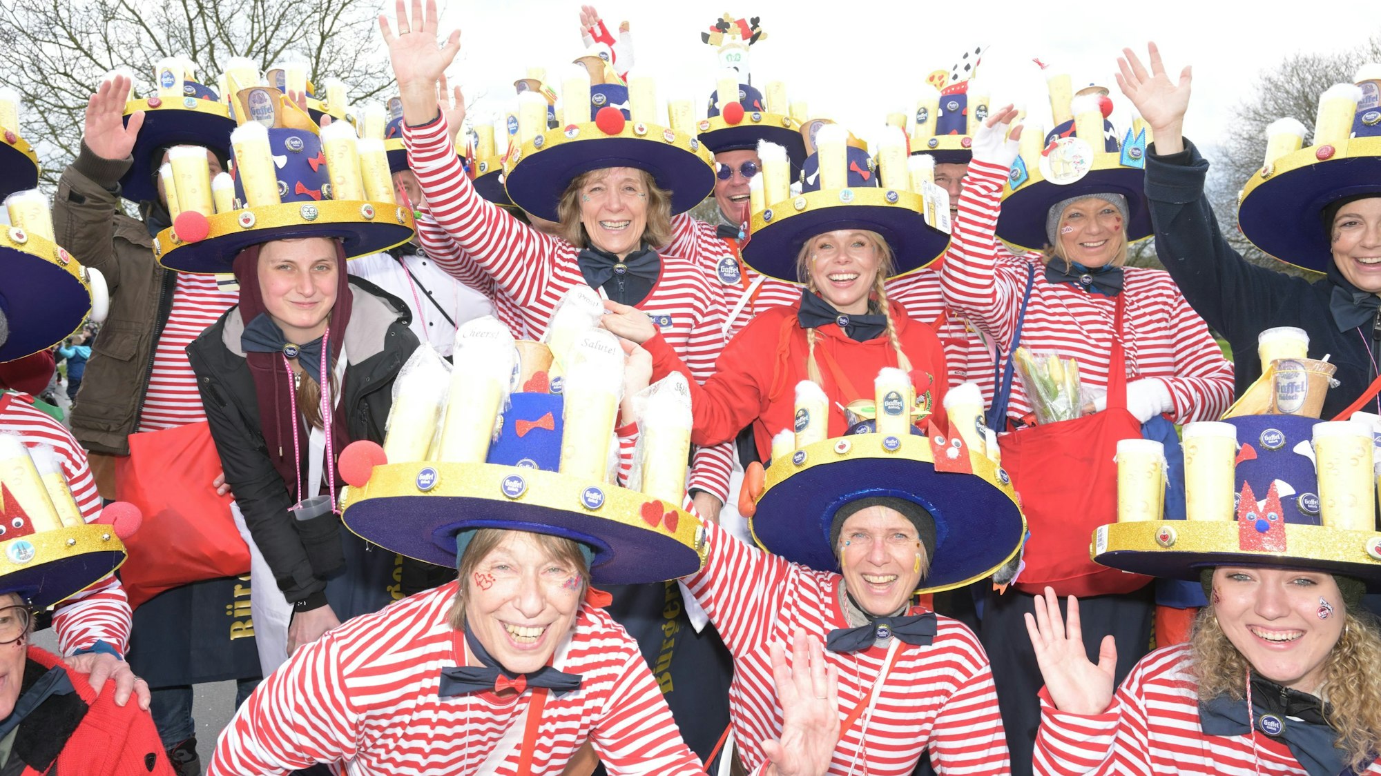 Eine Karnevalsgruppe mit Hüten, auf denen gefüllte Kölschgläser stehen.