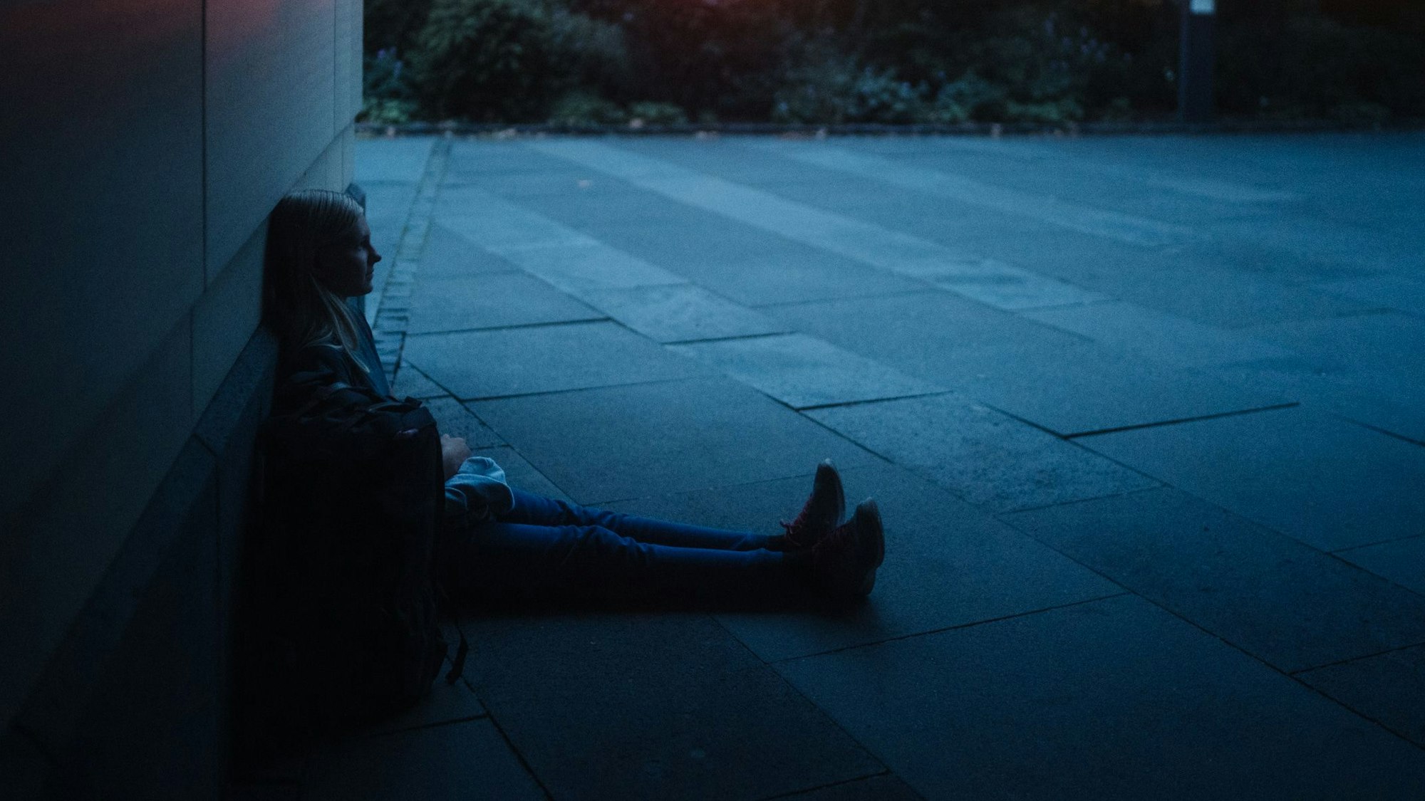 Ein junges Mädchen sitzt nachts an einer Hauswand auf der Straße.