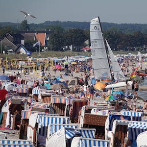 Passantinnen und Passanten genießen das Sonnenwetter am Strand der Ostsee.