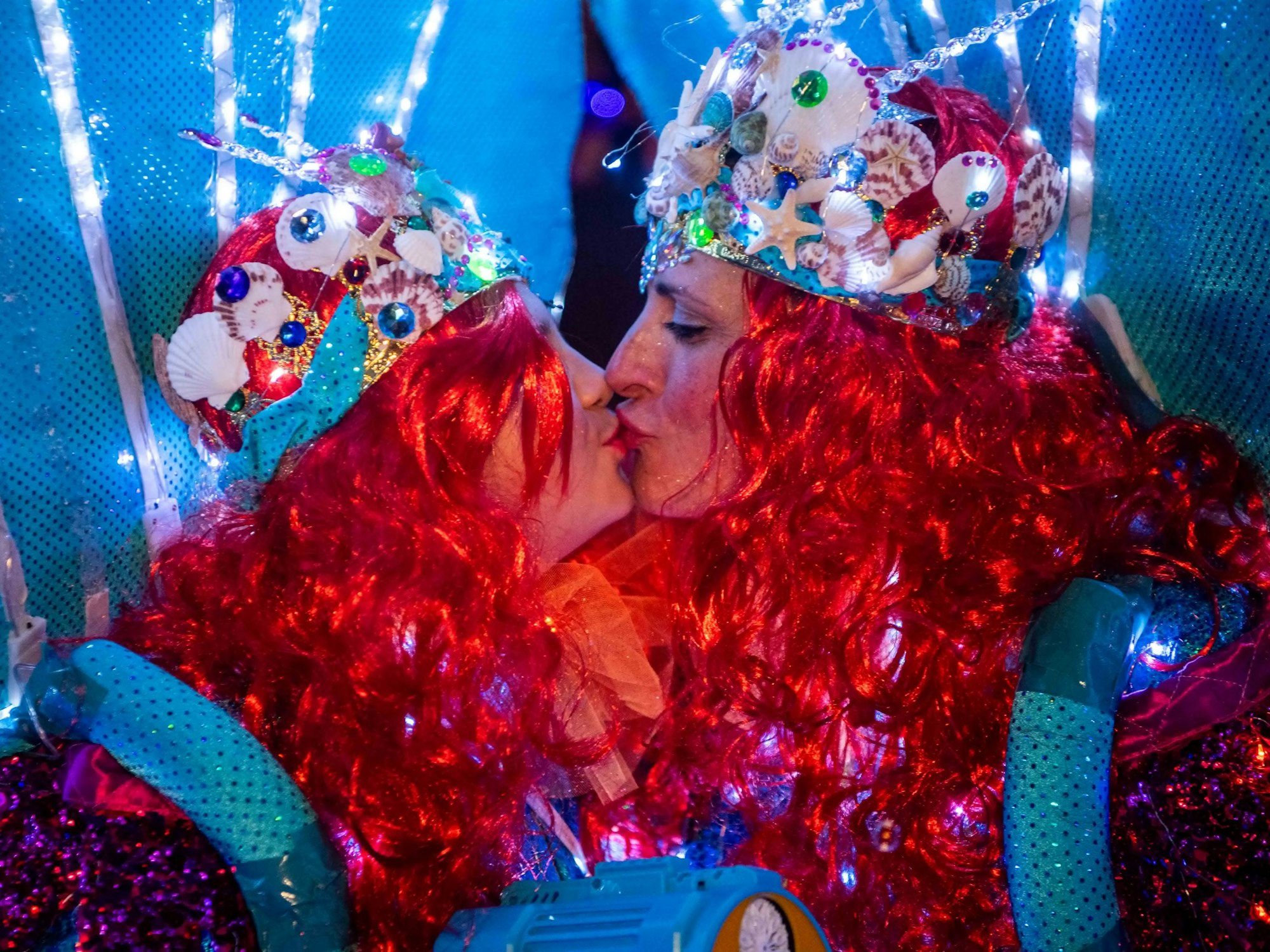 Das Bild zeigt zwei Frauen, die als Meerjungfrauen kostümiert sind und sich küssen.