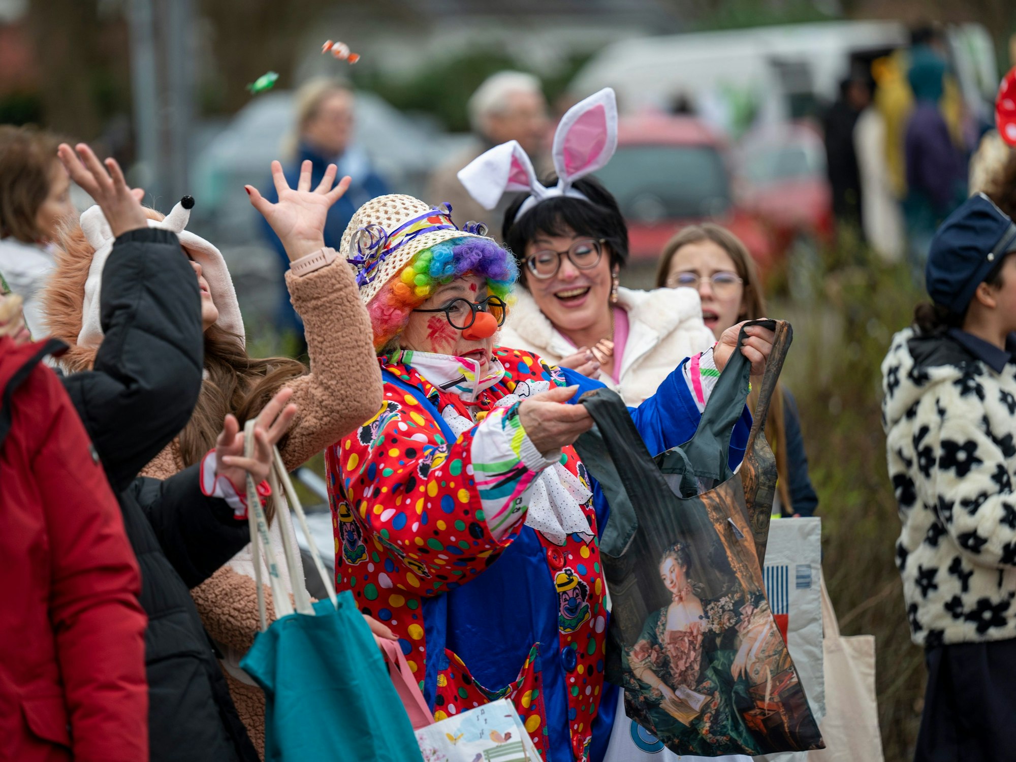 Eine Dame fängt, als Clown verkleidet, Kamelle beim Karnevalszug im Merheimer Veedel.