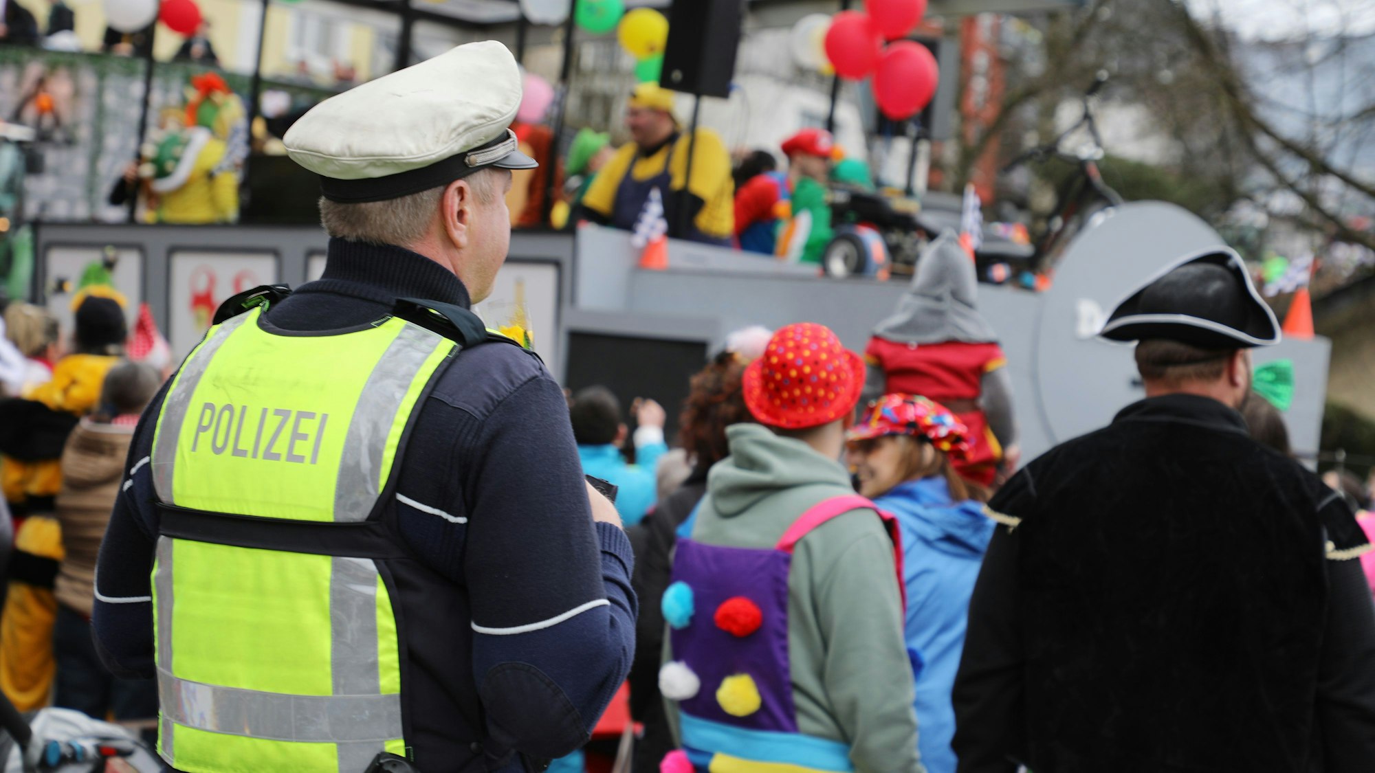 Ein Polizist steht am Rande des Kürtener Karnevalszugs und blickt auf das bunte Treiben.