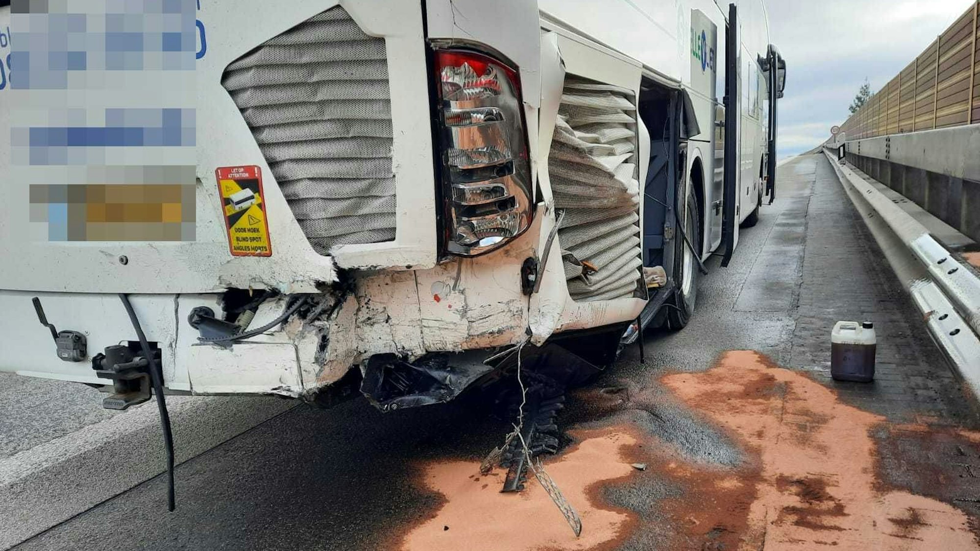 Ein weißer Reisebus mit beschädigtem Heck steht auf dem Standstreifen.