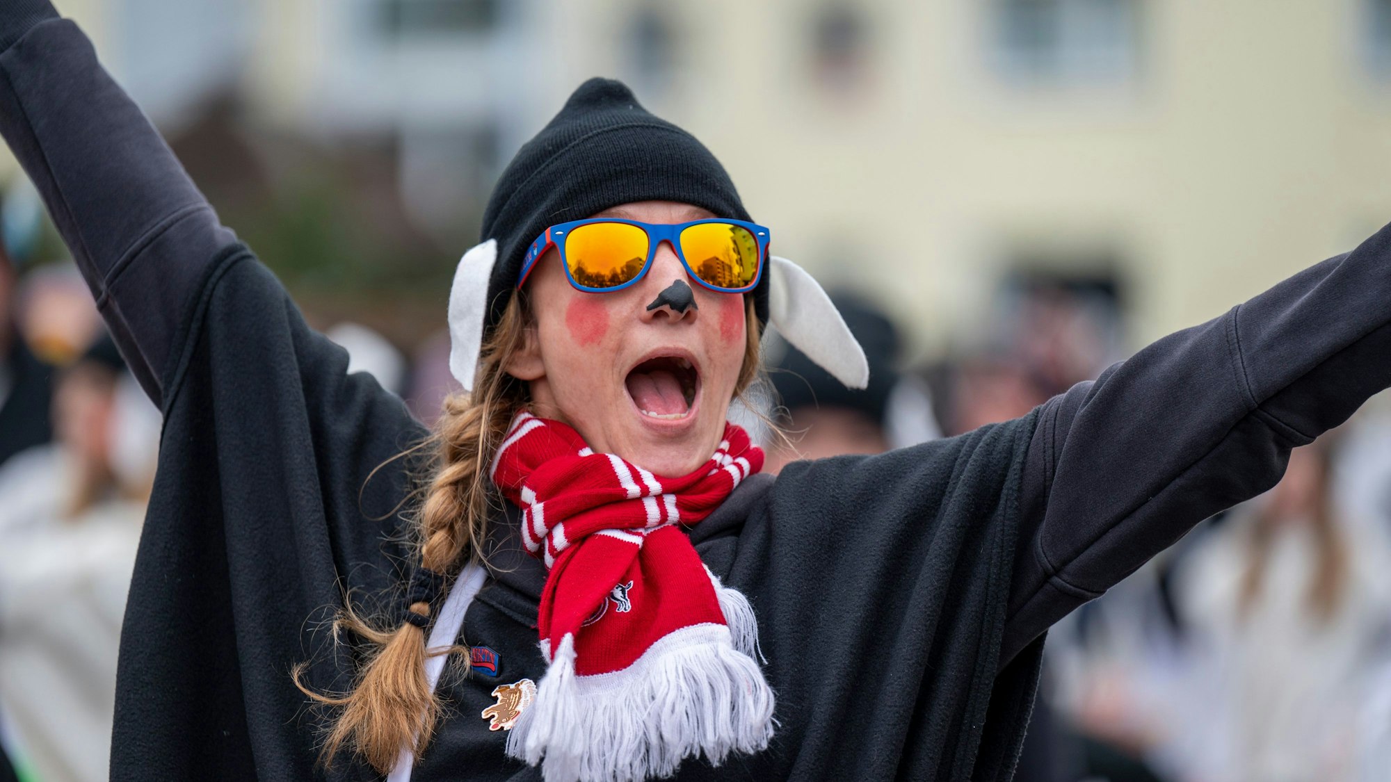 Die gute Laune war den Teilnehmenden beim Karnevalszug im Merheimer Veedel am 10. Februar anzusehen. Eine Frau in schwarzem Kostüm, mit Schal des 1. FC Köln und Sonnenbrille, jubelt.