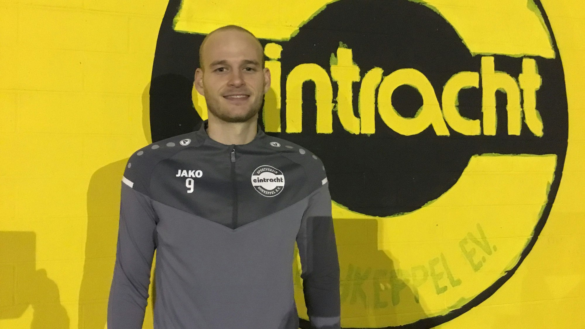 Fußballer Jannes Hoffmann steht vor einer gelben Wand mit dem Schriftzug „Eintracht“.