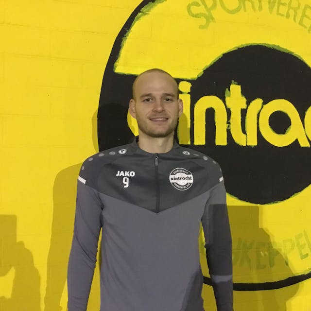 Fußballer Jannes Hoffmann steht vor einer gelben Wand mit dem Schriftzug „Eintracht“.