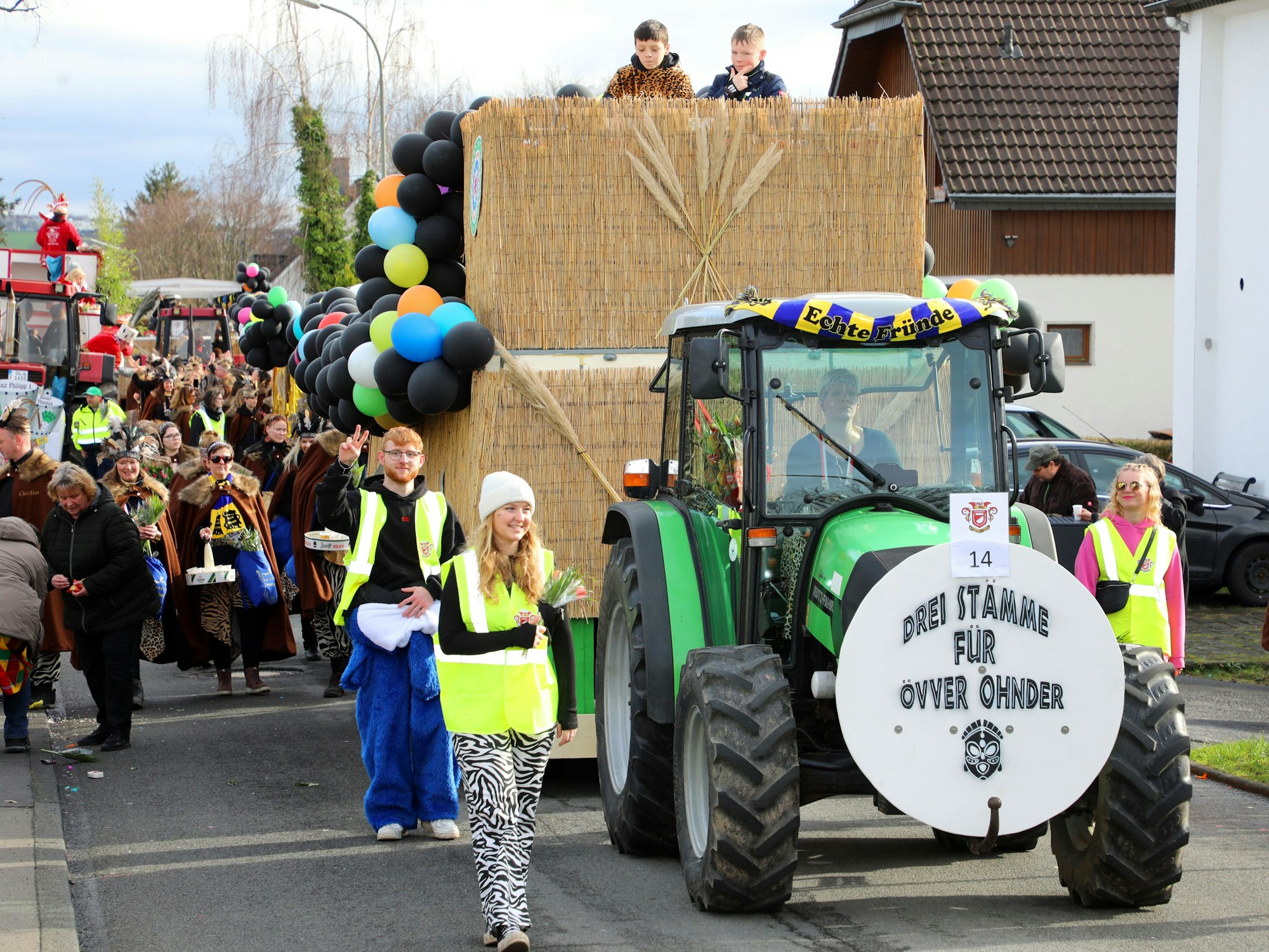 Ein Traktor zieht einen Karnevalswagen, vorne auf dem Traktor prangt ein rundes Schild mit der Aufschrift: „Drei Stämme für Oberodenthal“.