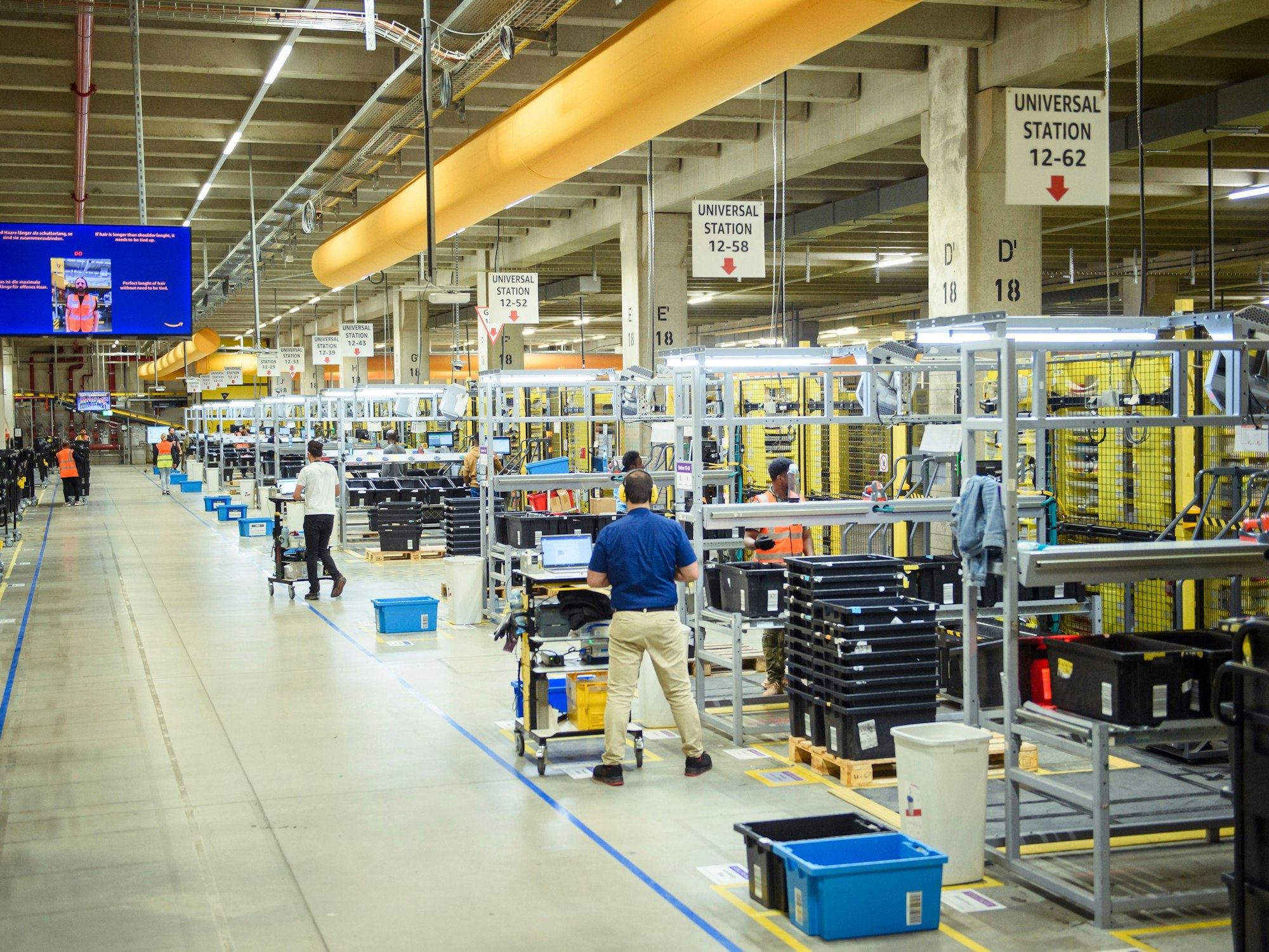 Mitarbeitende verpacken Waren im Logistikzentrum der Amazon Logistik GmbH in Winsen mithilfe von Scannern in passende Versandpakete, hier im Juli 2023.
