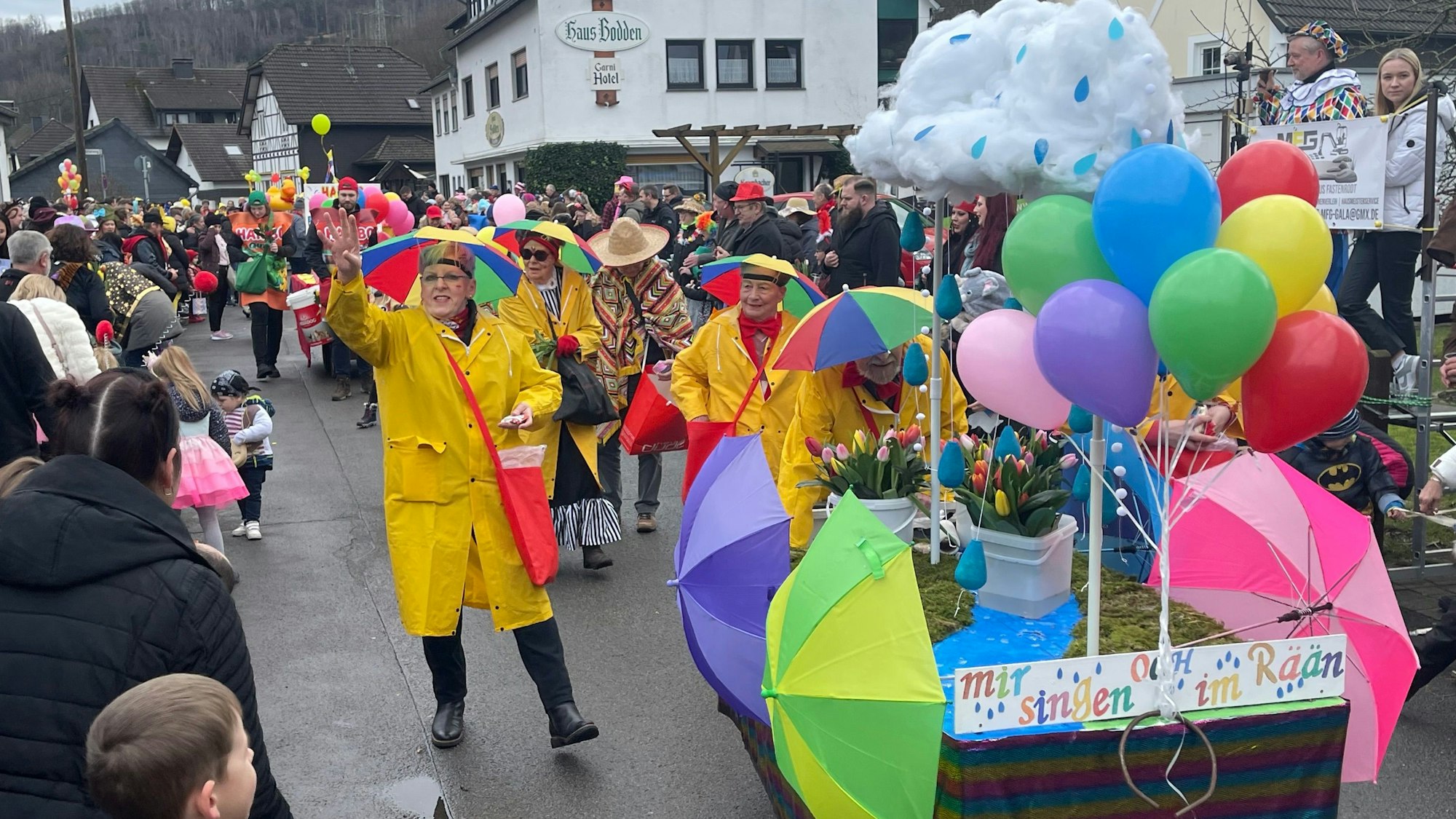Eine mit Regenjacken und Schirmen auf dem Kopf verkleidete Gruppe, verteilt beim Karnevalszug in Gummersbach-Rebbelroth Kamelle.