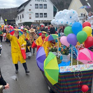 Eine mit Regenjacken und Schirmen auf dem Kopf verkleidete Gruppe, verteilt beim Karnevalszug in Gummersbach-Rebbelroth Kamelle.&nbsp;