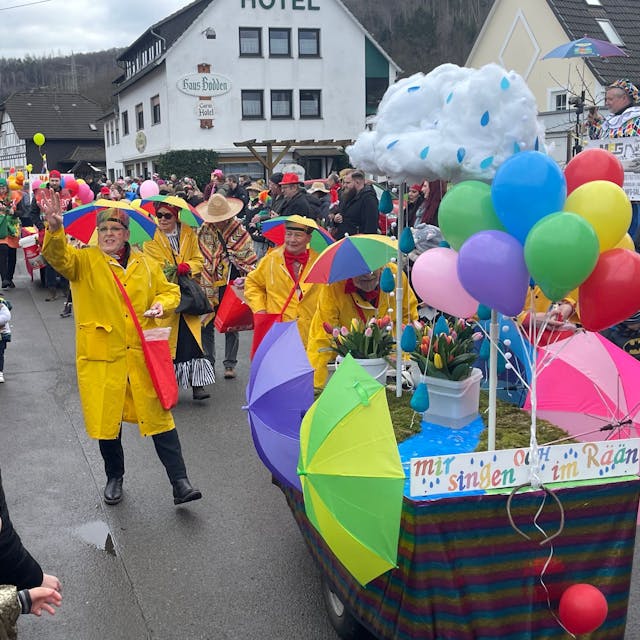 Eine mit Regenjacken und Schirmen auf dem Kopf verkleidete Gruppe, verteilt beim Karnevalszug in Gummersbach-Rebbelroth Kamelle.&nbsp;