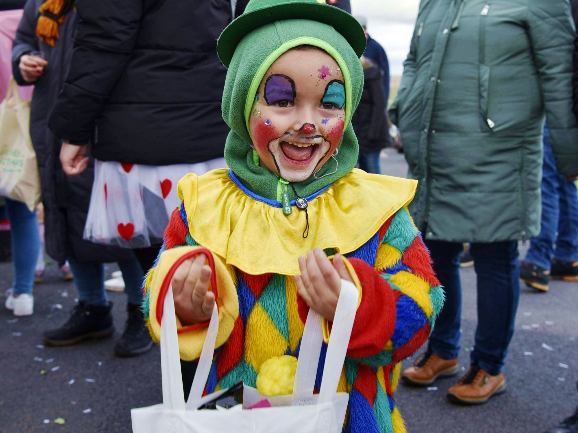 Ein als Clown verkleideter Junge steht mit Tüte am Straßenrand.