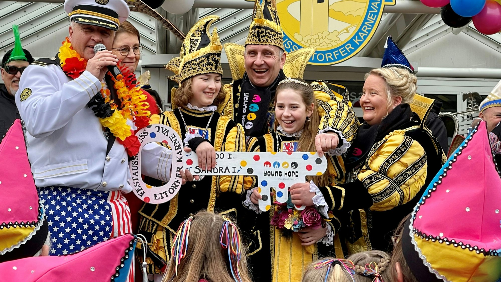 Ein Kinderprinzenpaar und ein erwachsenes Paar in prunkvollen schwarz-gelben Kostümen stehen lachend auf der Treppe zum Rathaus und halten einen großen Schlüssel in der Hand, die ihnen ein als Kapitän verkleideter Bürgermeister Rainer Viehof übergibt.