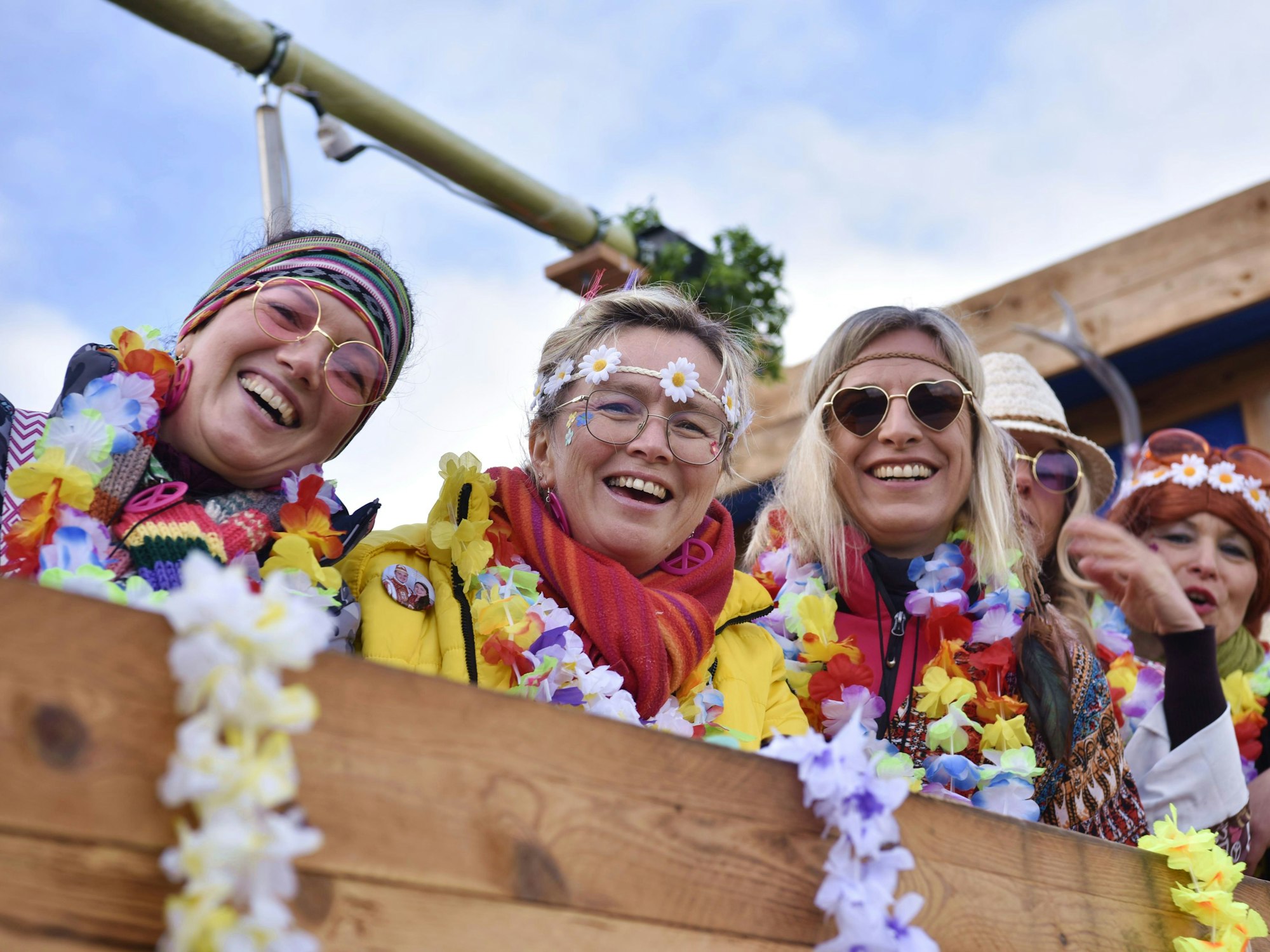 Drei Frauen als Hippies verkleidet, lachen von einem Karnevalswagen aus in die Kamera.