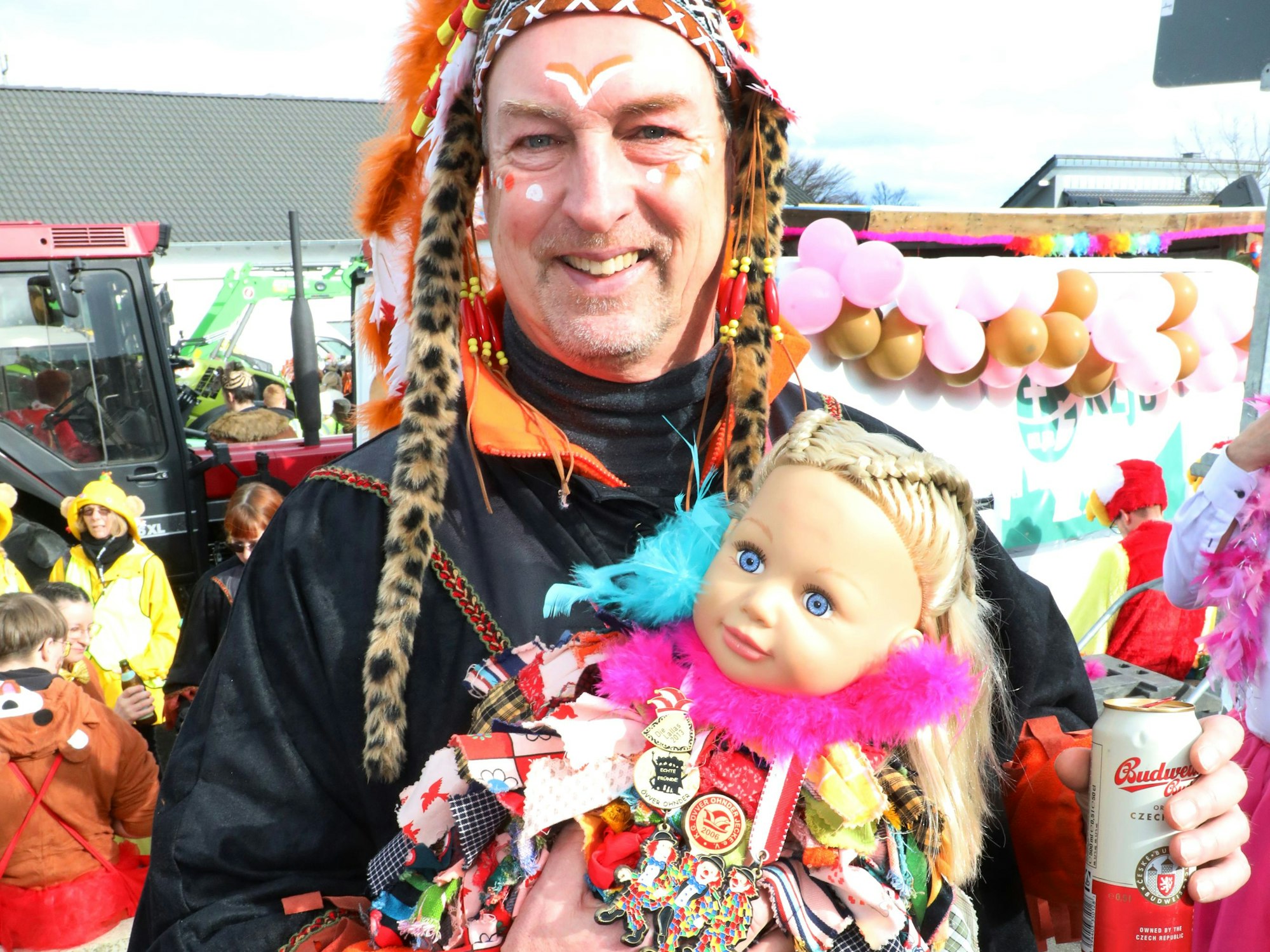 Ein als Indigener verkleideter Mann hält eine kostümierte Puppe im Arm.