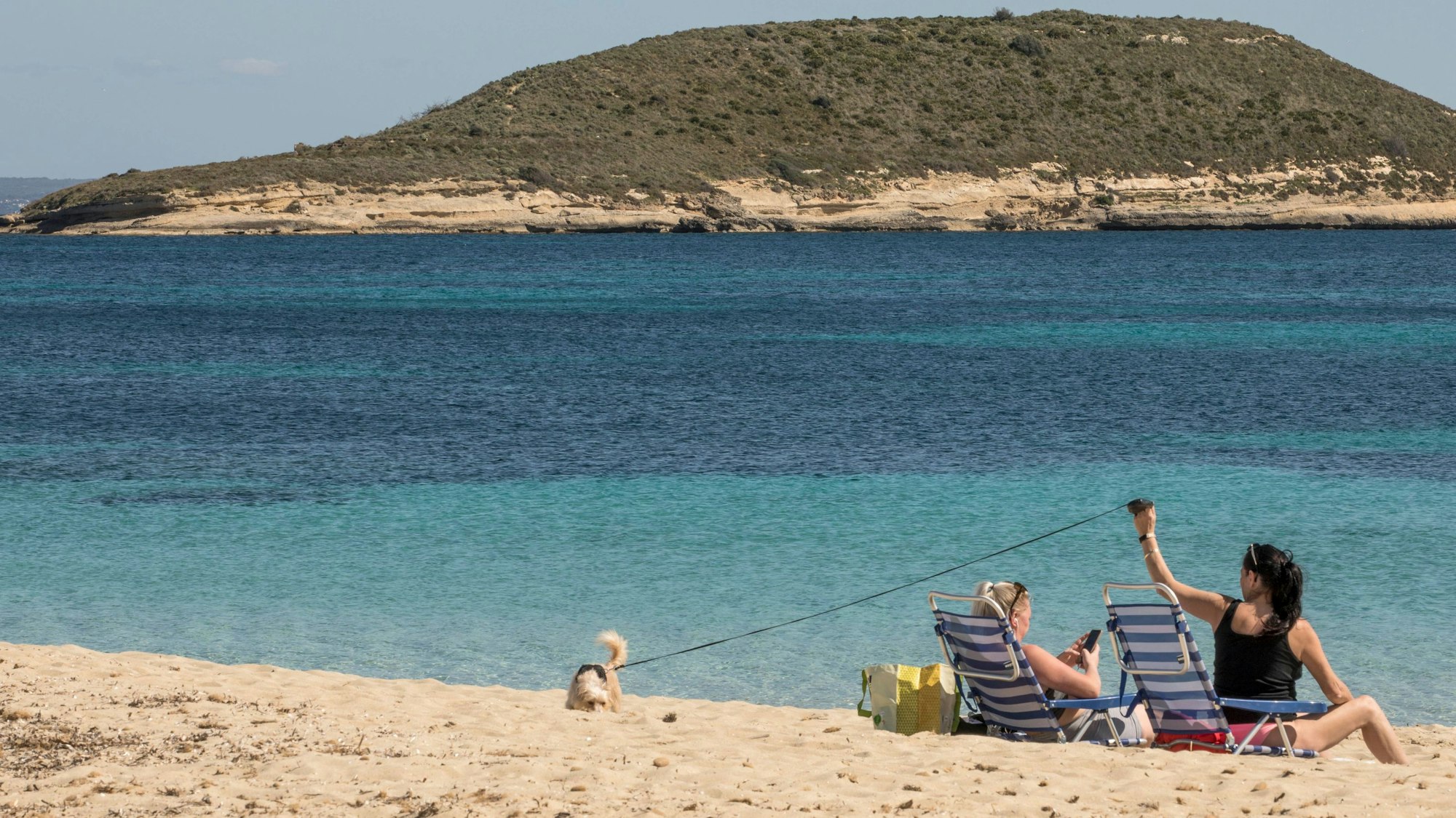 Zwei Frauen mit Hund liegen in Liegestühlen am Strand von Mallorca