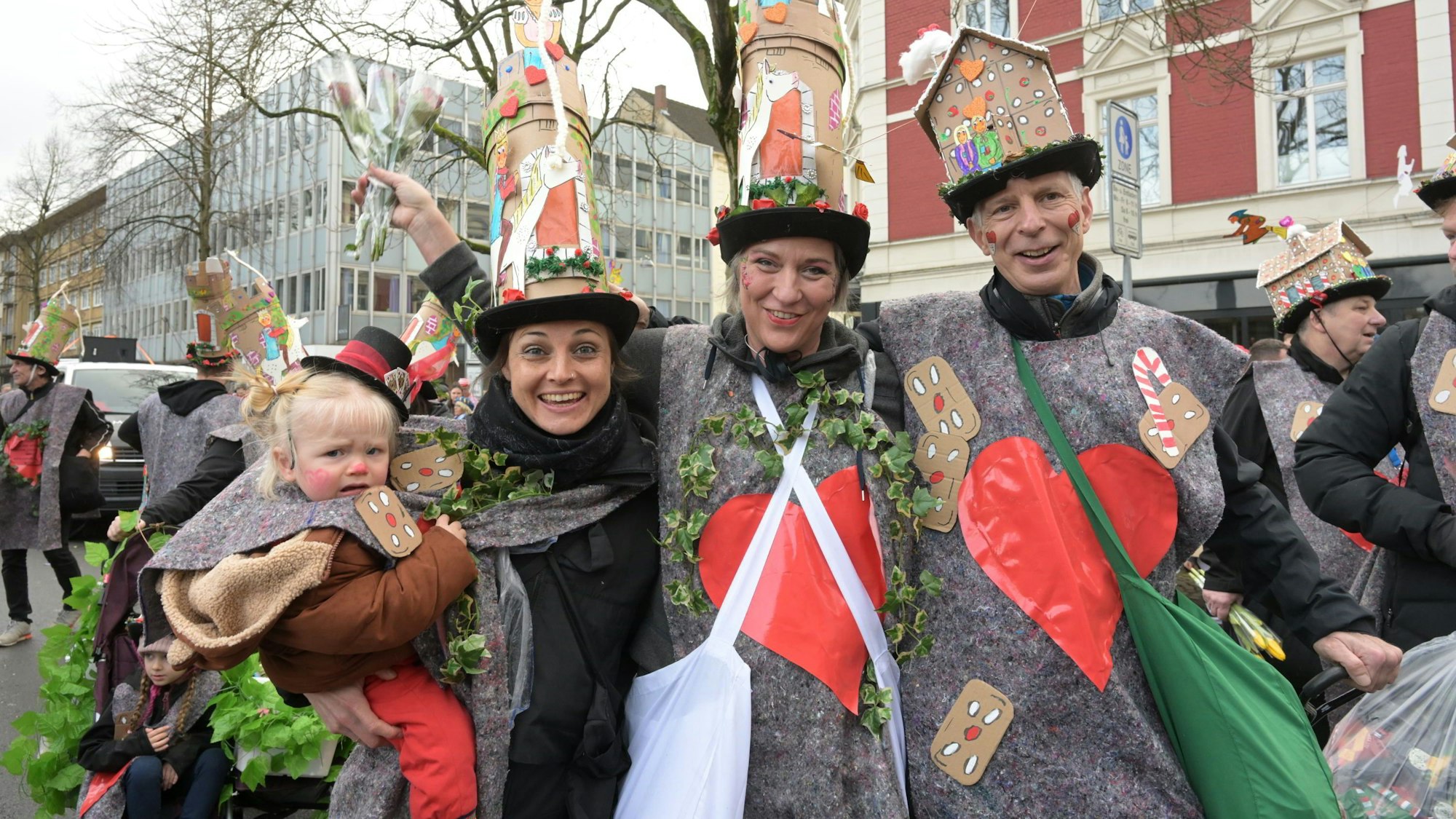 Menschen mit fantasievollen Kostümen und hohen Hüten feiern auf der Straße.