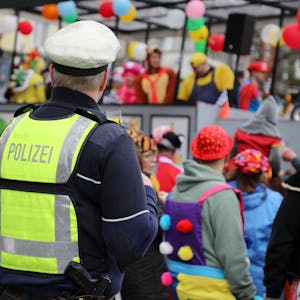 Ein Polizist steht an einem Karnevalszug und beobachtet das jecke Treiben.