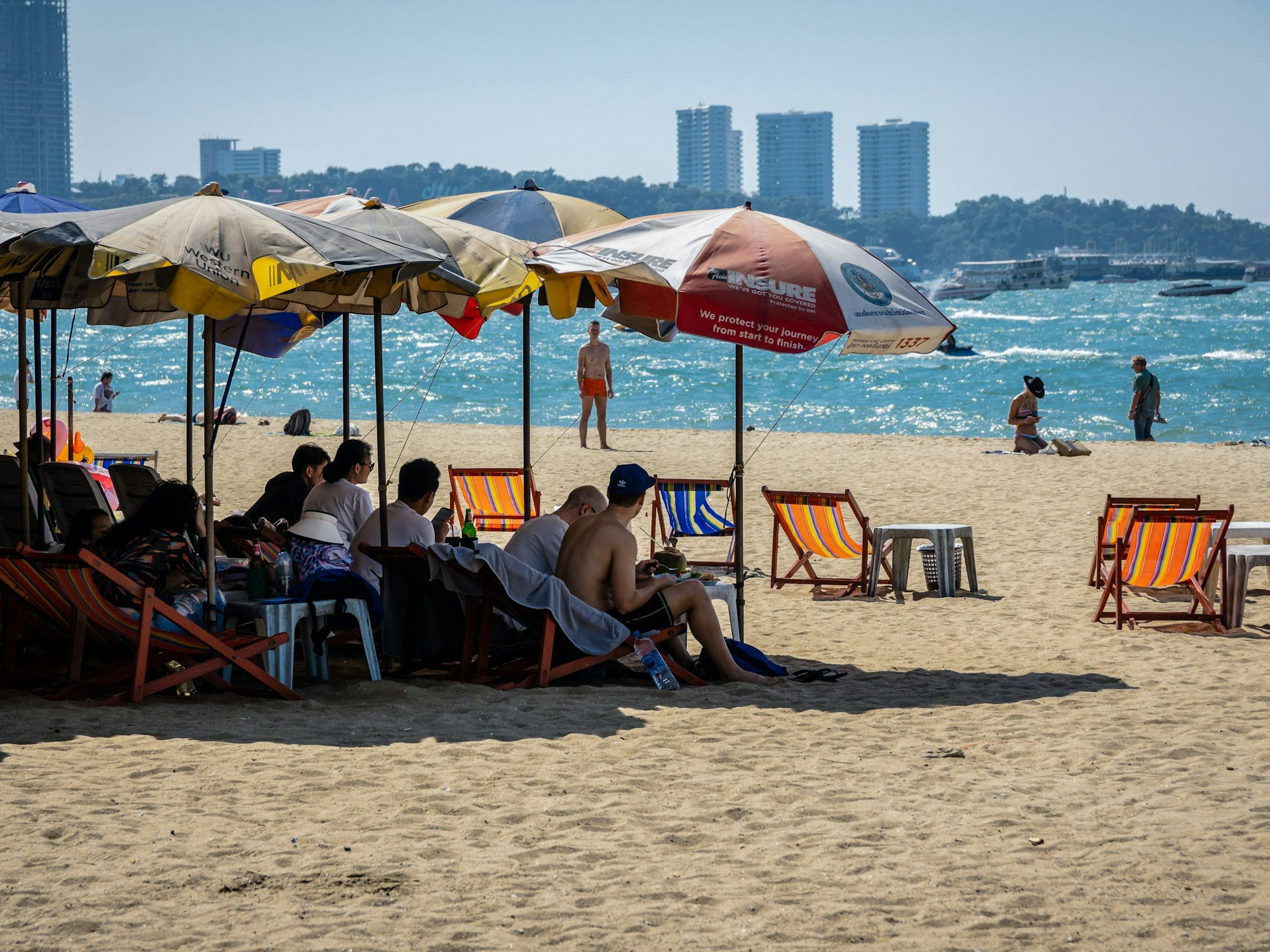 Touristen und Touristinnen auf Liegestühlen unter Sonnenschirmen am Strand von Pattaya in Thailand