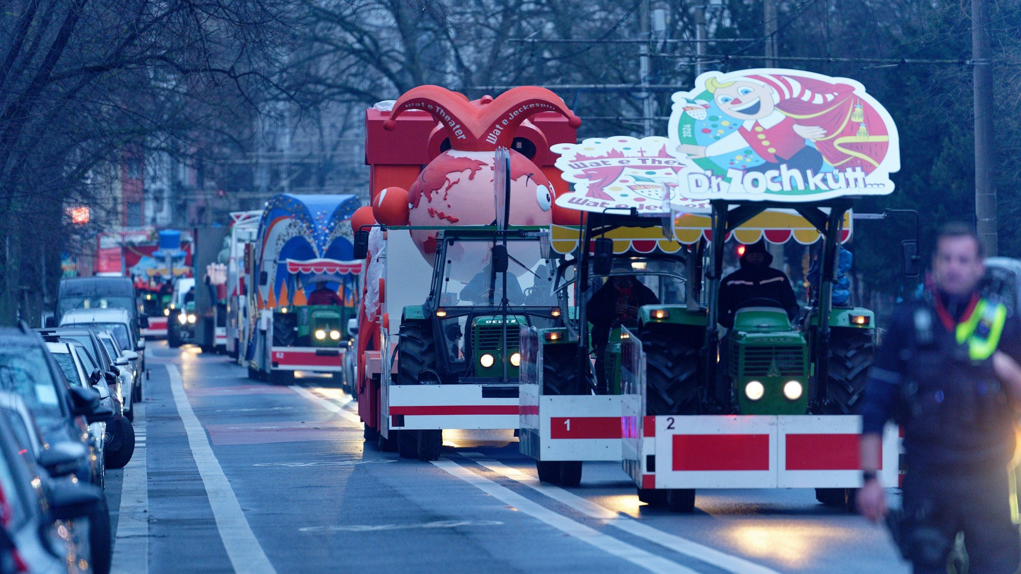 Einige Traktoren hintereinander fahren die Wagen des Kölner Rosenmontagszugs durch die Stadt.