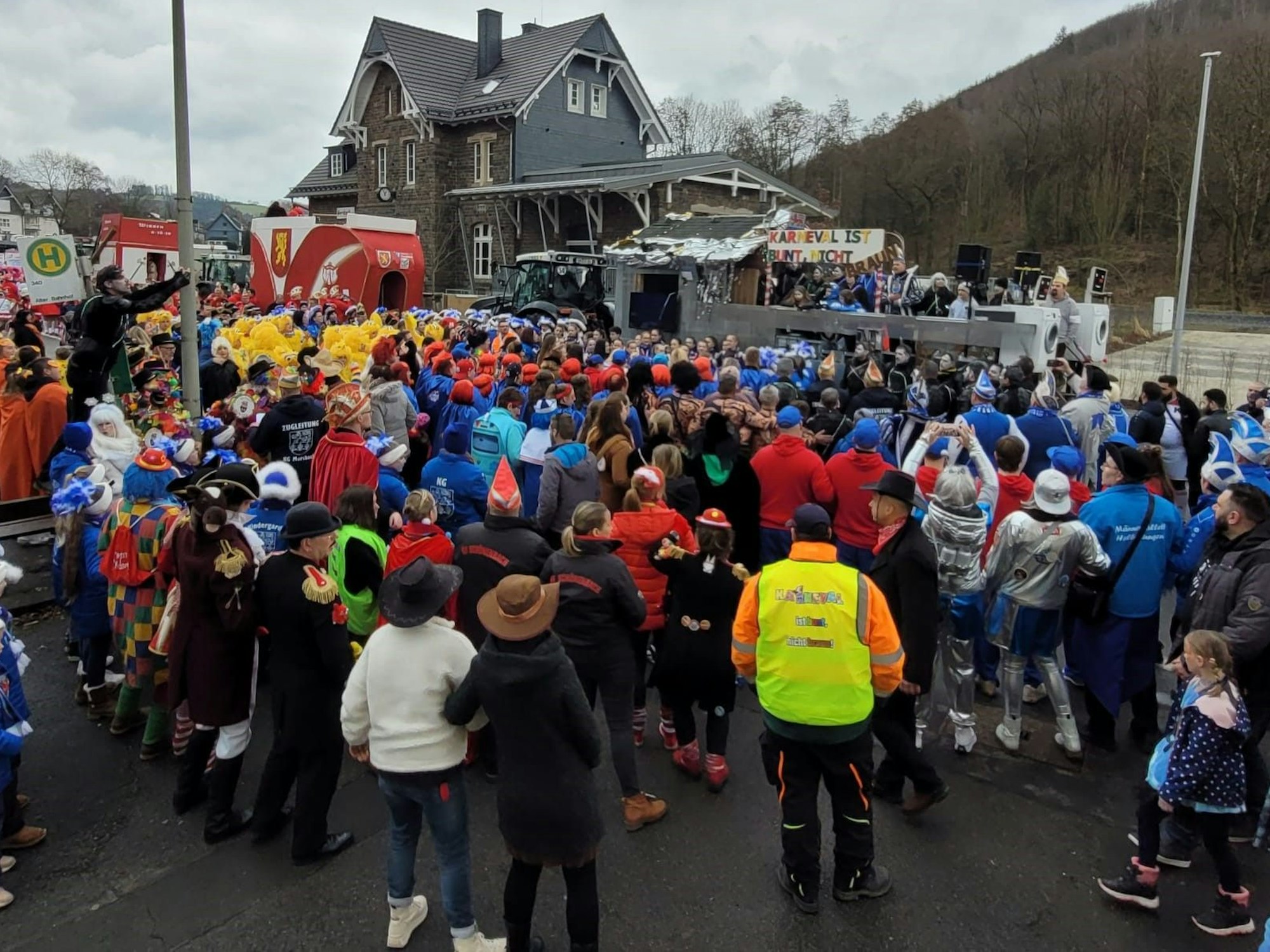 Zahlreiche Menschen stehen vor dem Prinzenwagen in Morsbach beisammen. Auf diesem ist ein Schild zu sehen, auf dem steht: „Karneval ist bunt, nicht braun“.
