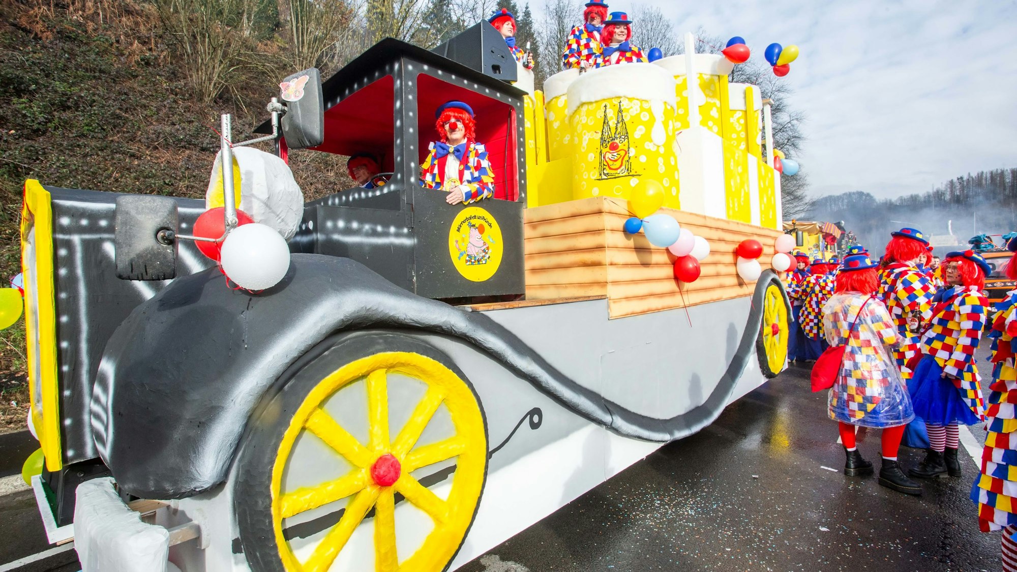 Ein Karnevalswagen im Stile eines Oldtimer-Lkw mit großen Kölschstangen inmitten feiernder Menschen.