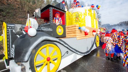 Ein Karnevalswagen im Stile eines Oldtimer-Lkw mit großen Kölschstangen inmitten feiernder Menschen.