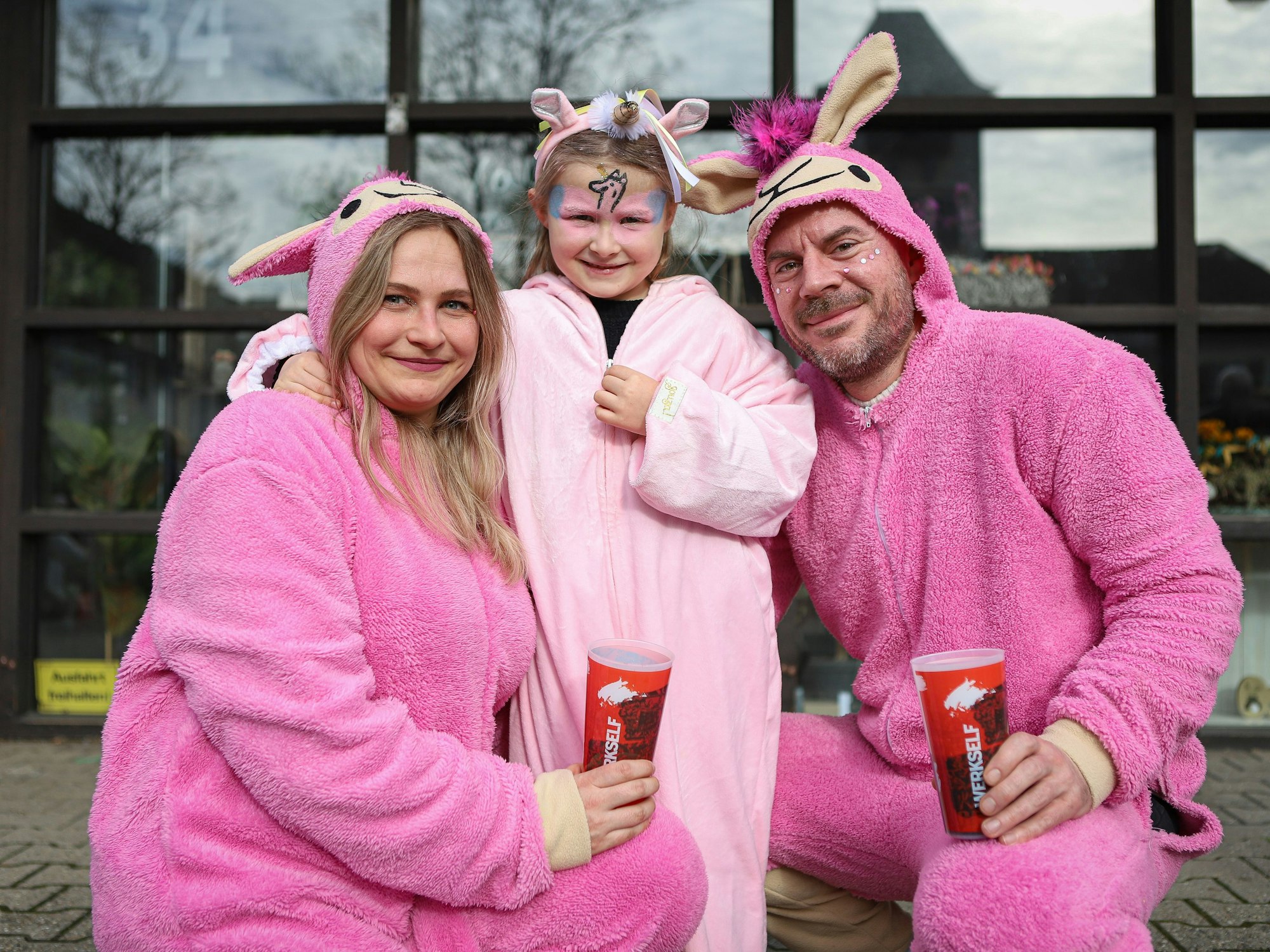 Ein Mädchen und ihre Eltern in rosa Kostümen als Alpakas und ein Einhorn.
