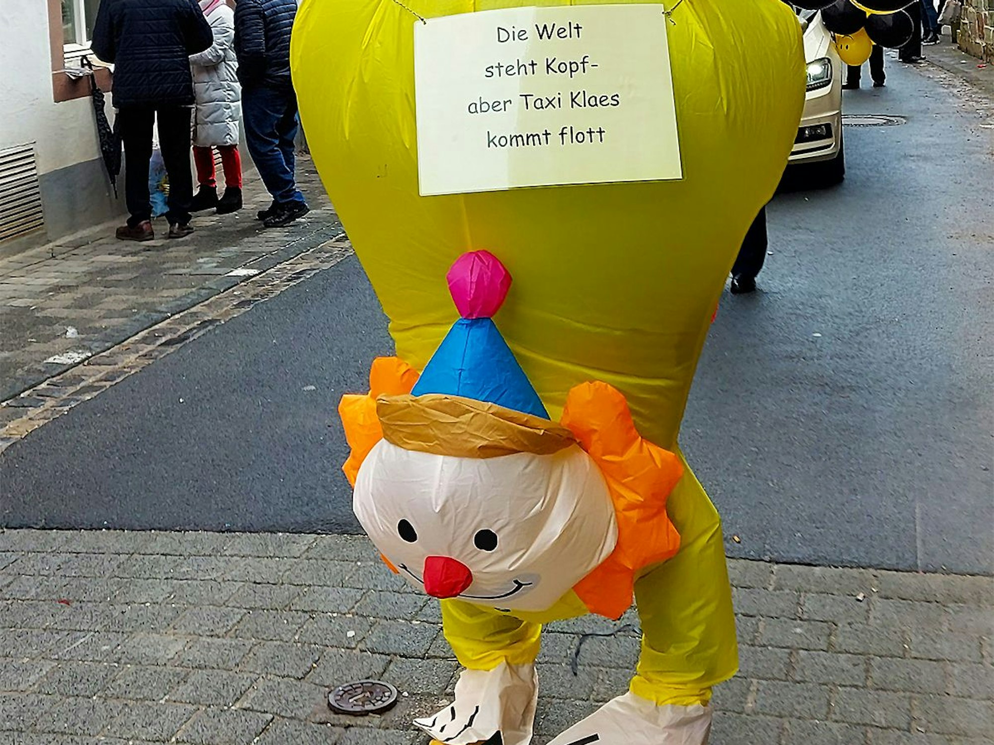 Clown auf Händen: „Die Welt steht Kopf“, doch auf das örtliche Taxiunternehmen ist Verlass.