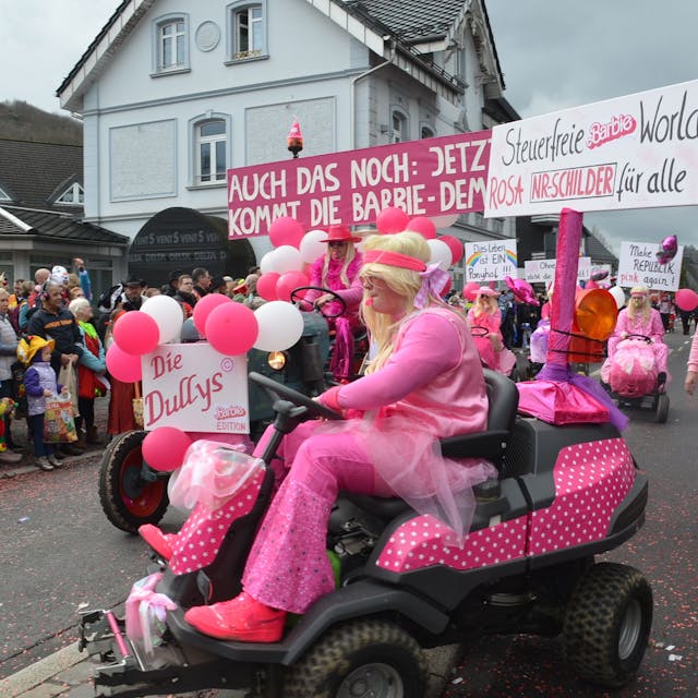Als Barbie verkleidete Jecke sind bei einem Umzug auf rosafarbenen Sitzrasenmähern unterwegs.