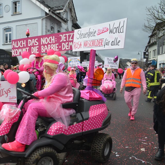 Als Barbie verkleidete Jecke sind bei einem Umzug auf rosafarbenen Sitzrasenmähern unterwegs.