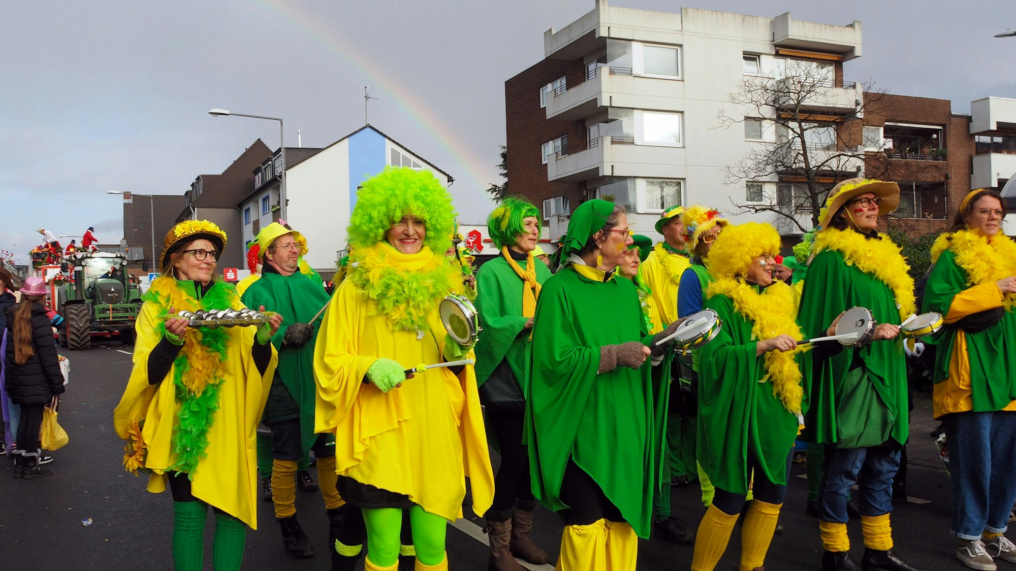 Eine grün-gelbe Sambagruppe tanzt unterm Regenbogen.
