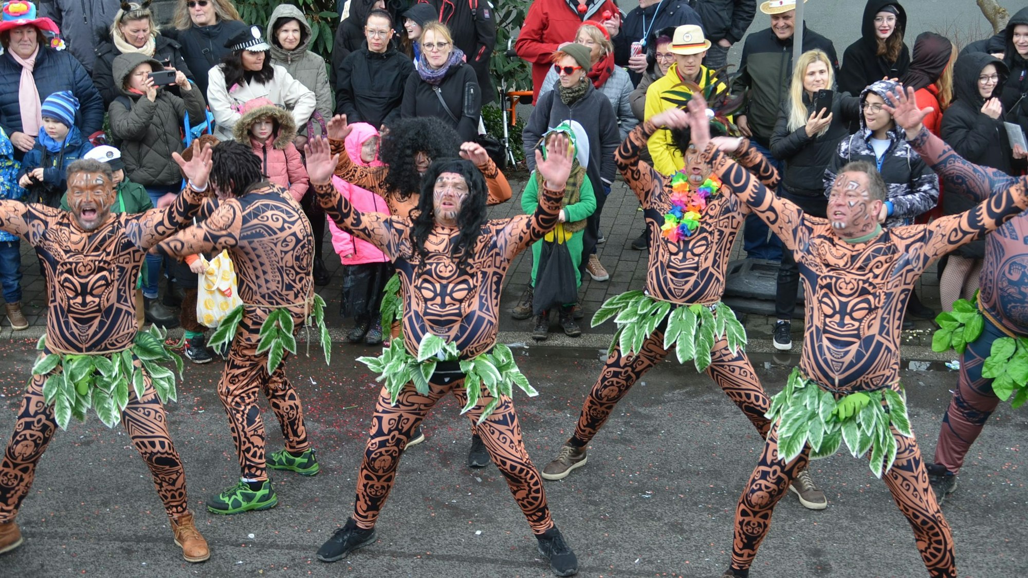 Eine Karnevalsgruppe, mit Röcken aus grünen Blättern verkleidet, tanzt auf der Straße.