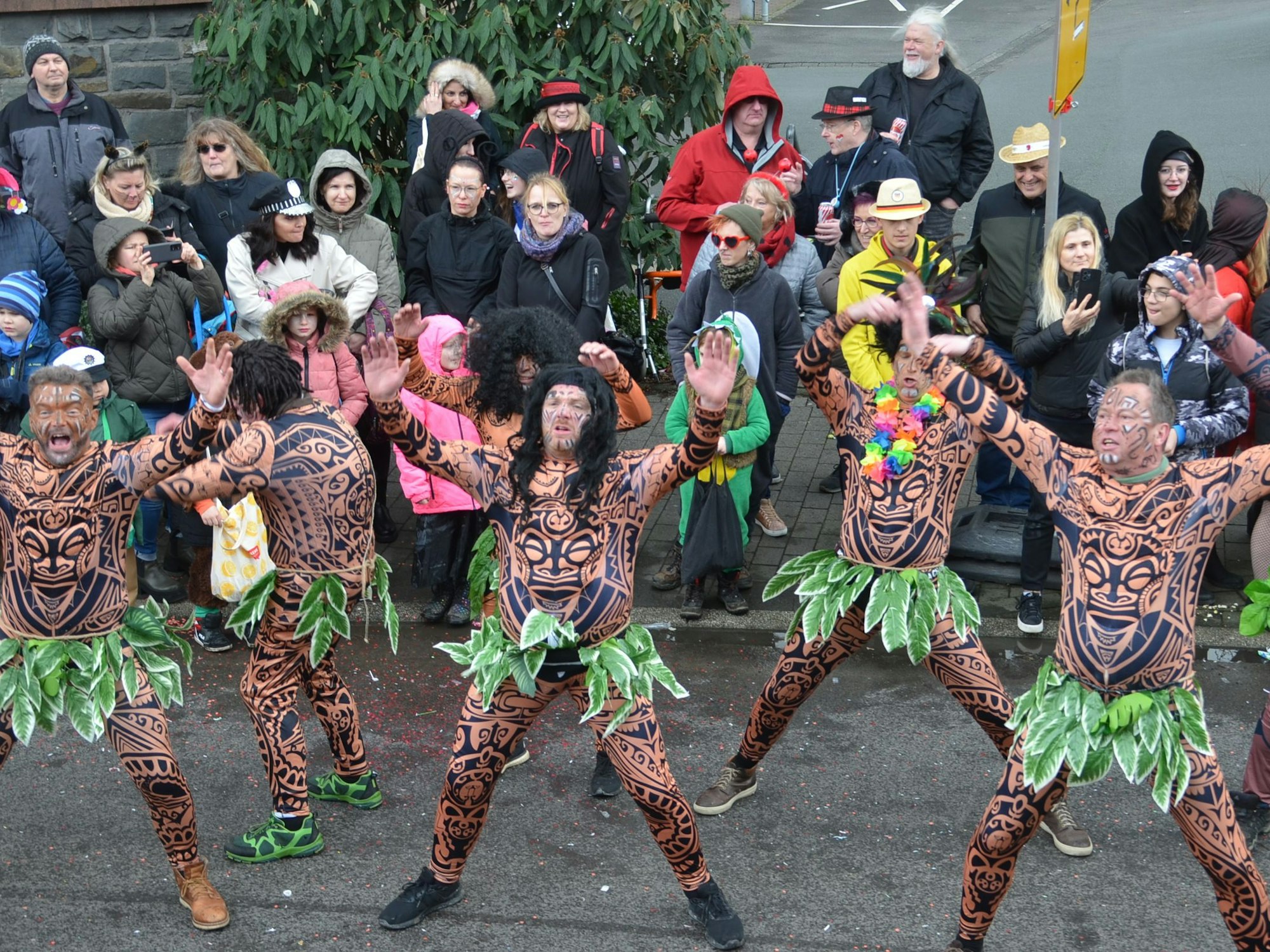 Eine Karnevalsgruppe, mit Röcken aus grünen Blättern verkleidet, tanzt auf der Straße.