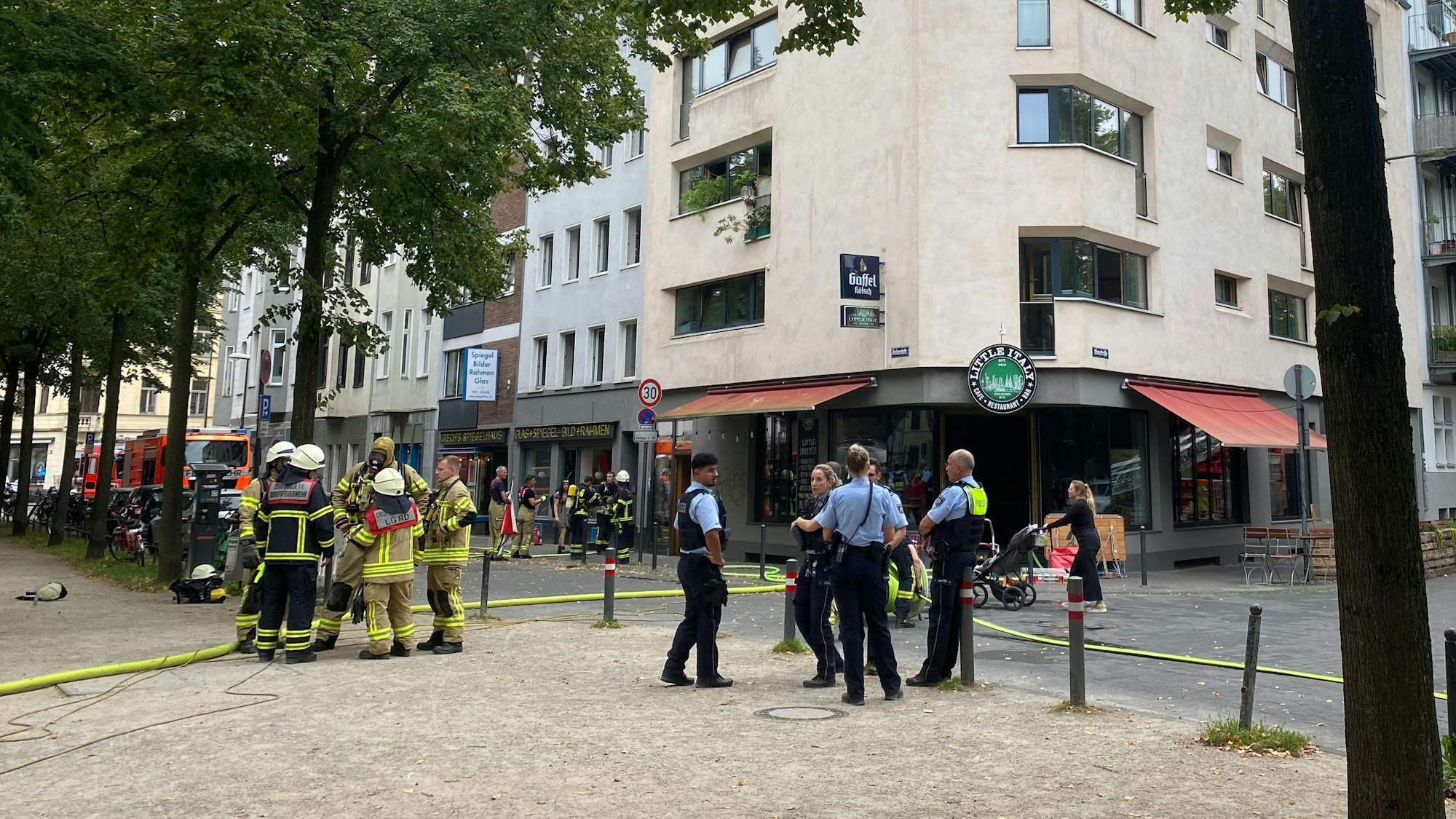 Einsatzkräfte von Feuerwehr und Polizei stehen bei einem Brand in Köln auf der Straße.