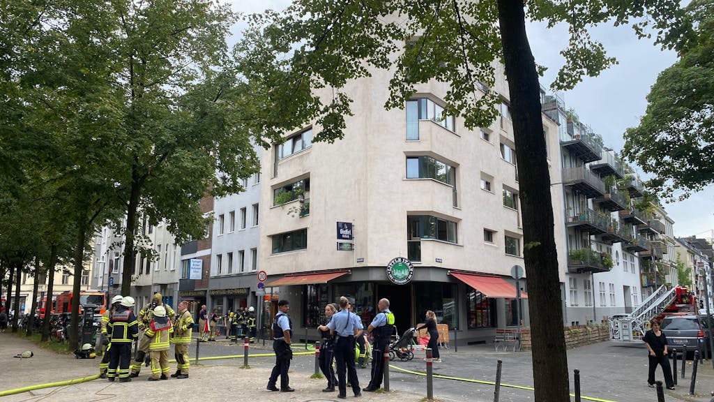 Einsatzkräfte von Feuerwehr und Polizei stehen bei einem Brand in Köln auf der Straße.