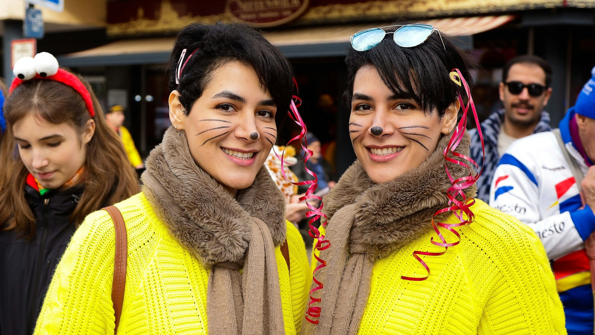 Zwei Zuschauerinnen beim Südstadtzug in gelben Pullovern und mit geschminkten Katzenschnurrhaaren.