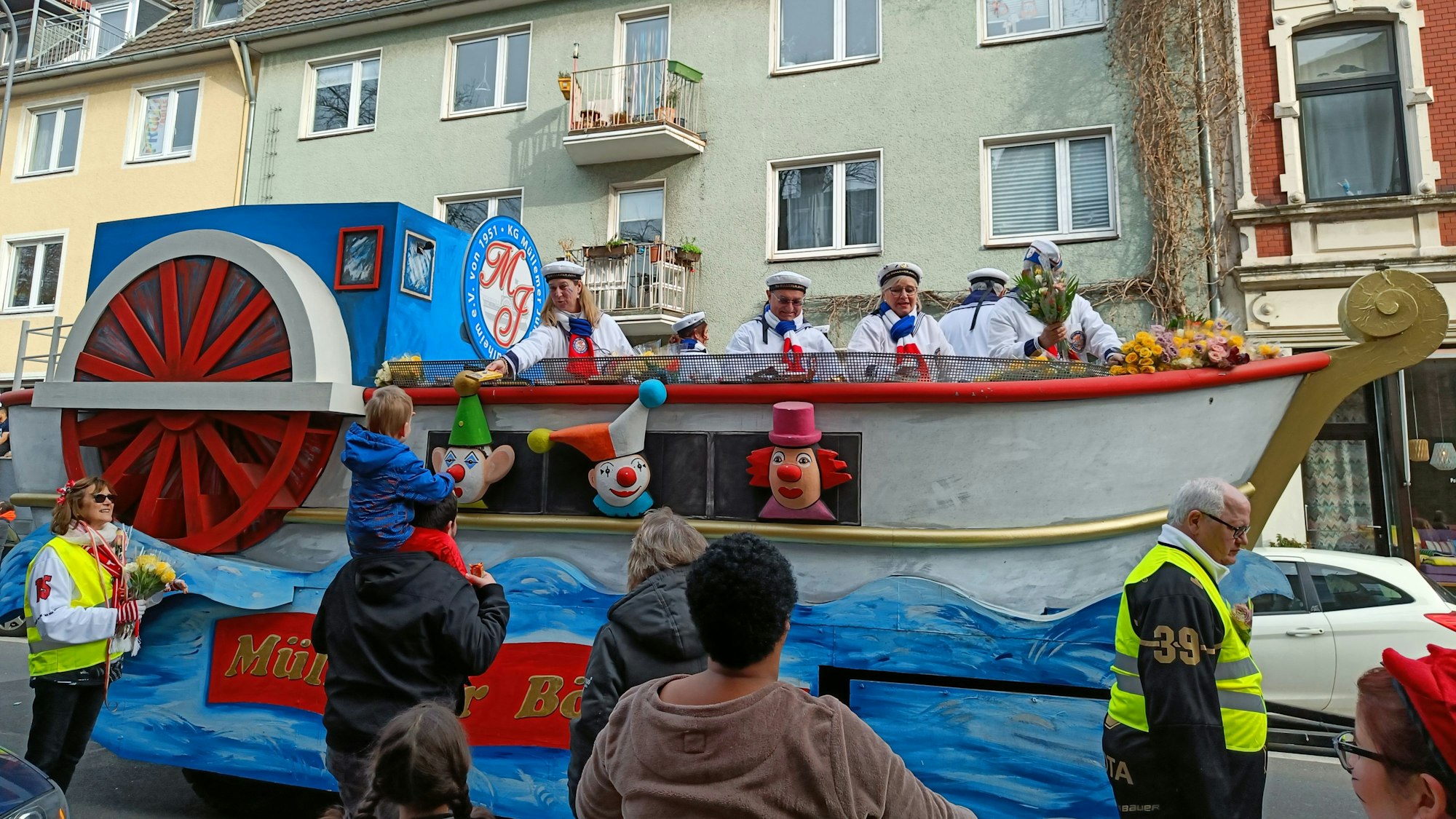 Karnevalisten reichen Kamelle von einem Schaufelradboot herunter.