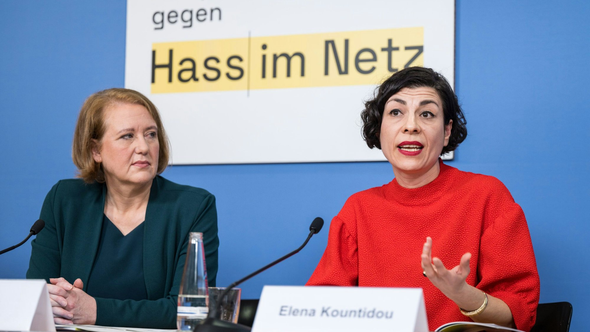 Lisa Paus und Elena Kountidou sitzen an einem Tisch, vor ihnen stehen Namensschilder und Mikrofone auf dem Tisch. Im Hintergrund die Aufschrift "gegen Hass im Netz".