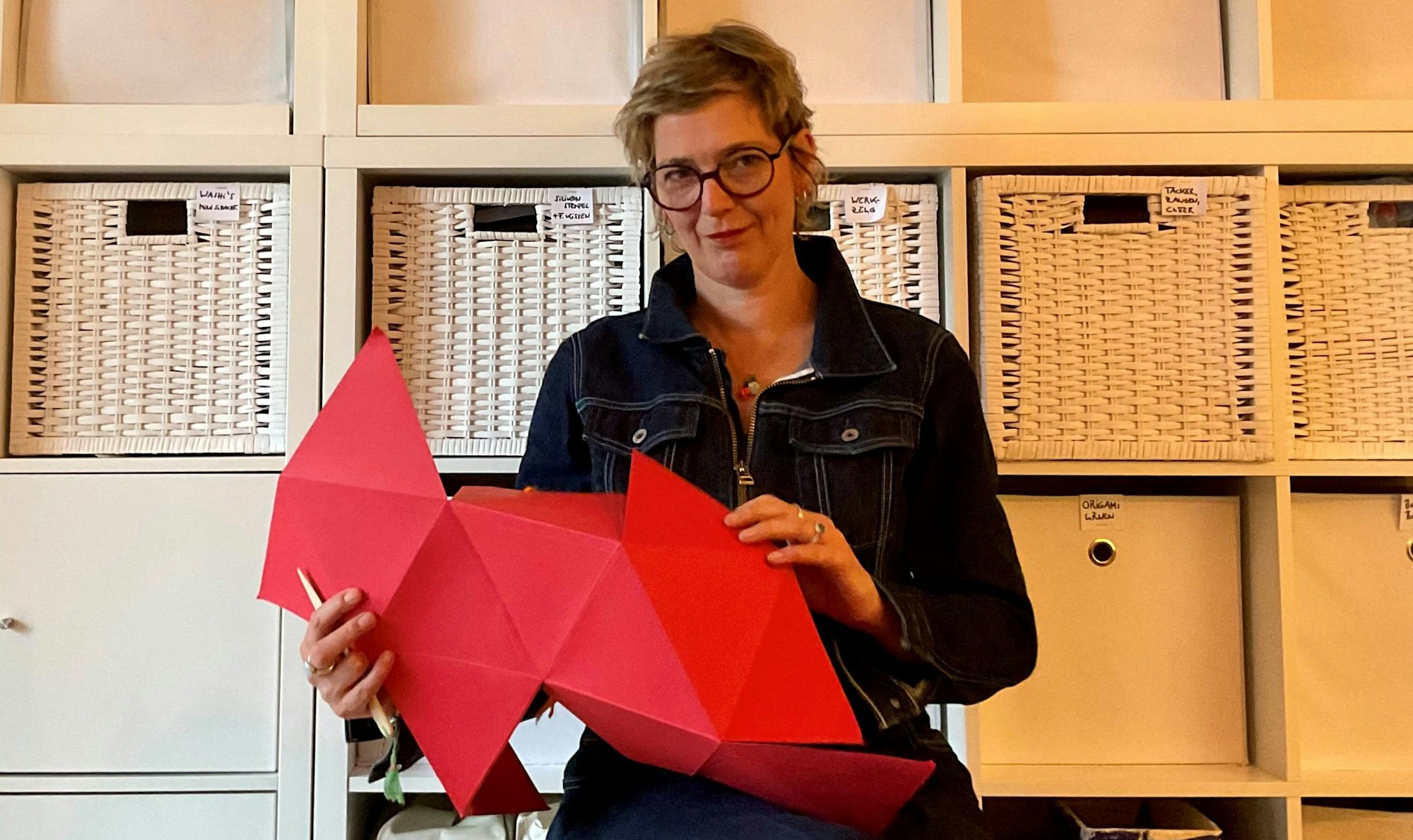 Eine Frau faltet einen großen roten Papierbogen auf Origami-Art