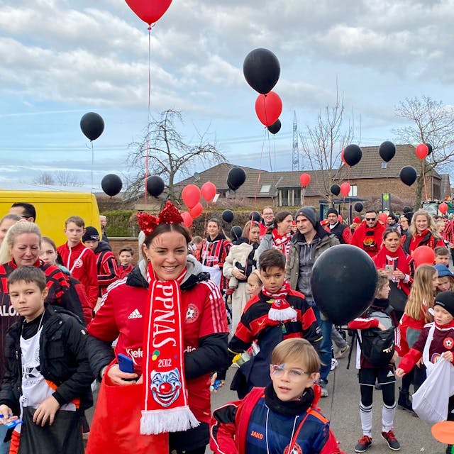Kinder und Jugendliche in Fußballtrikots und mit schwarzen und roten Ballons in den Händen.