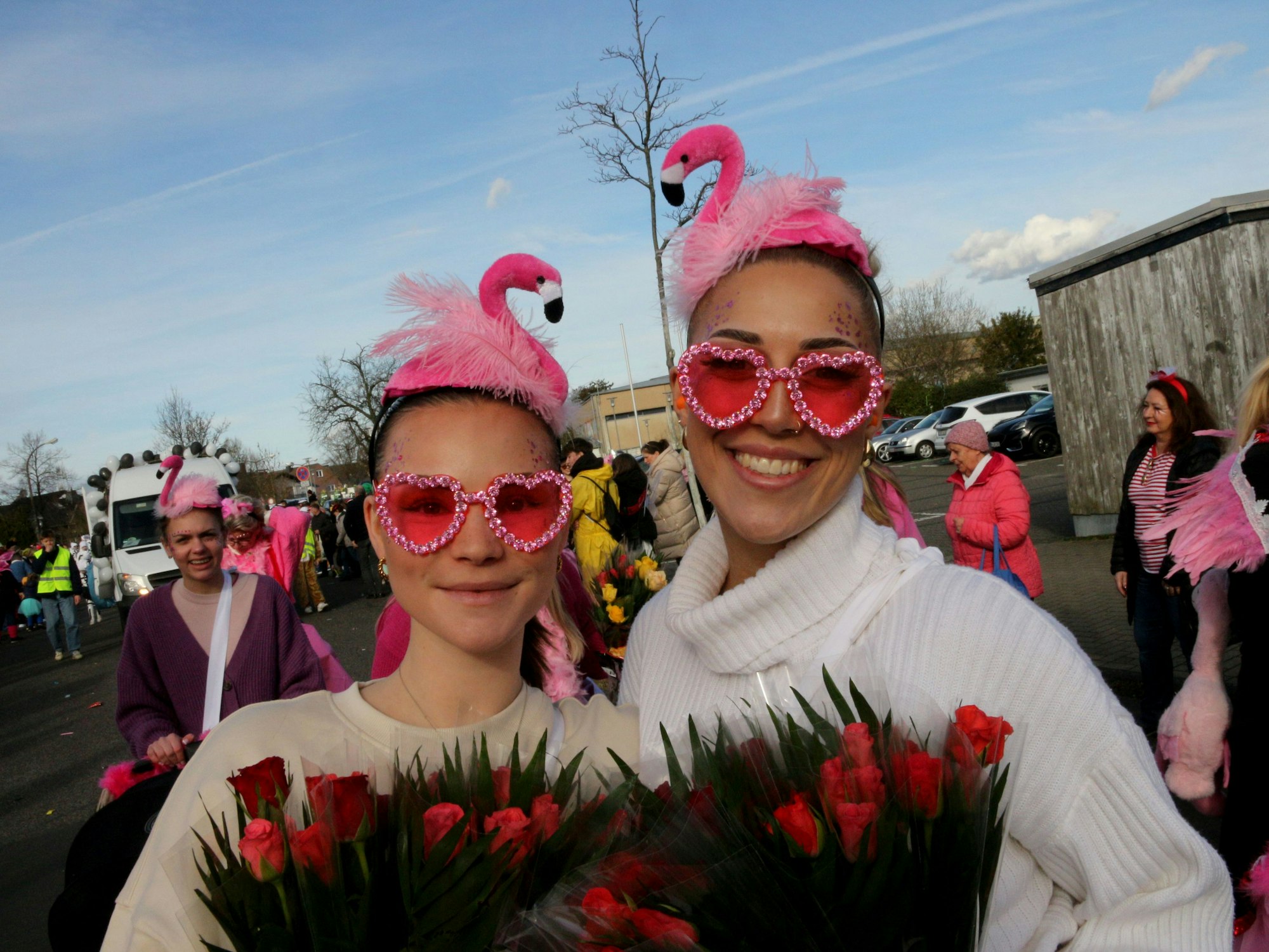 Zwei Frauen tragen rosafarbene Brillen, auf dem Kopf tragen sie rosafarbene Hüte mit zierlichen Flamingos.