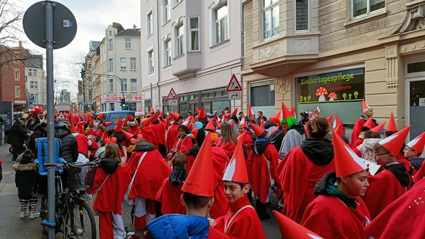 Kinder in roten Kostümen und Spitzhüten stehen als Teil des Veedelszugs auf einer Mülheimer Straße.