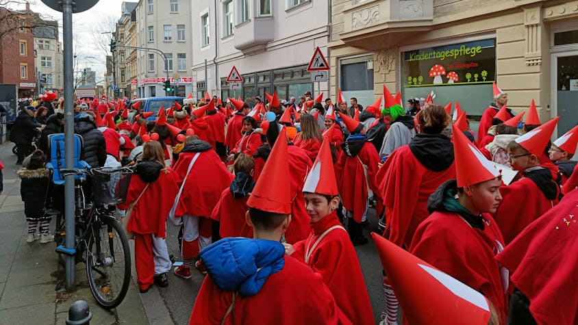 Kinder in roten Kostümen und Spitzhüten stehen als Teil des Veedelszugs auf einer Mülheimer Straße.