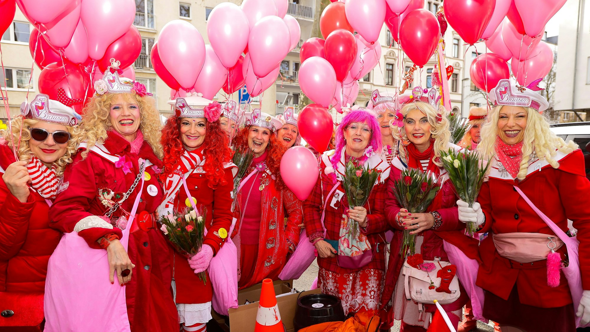 Eine Frauengruppe in roten Jacken und Mänteln ist mit pinken Luftballongs ausgestattet.