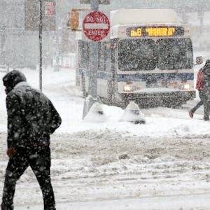 Passanten gehen bei starkem Schneefall über eine Straße in New York, im Hintergrund fährt ein Bus durch den massiven Schneefall. (Archivbild)