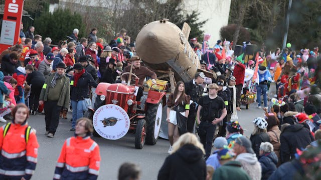 Ein roter Traktor, der eine Holz-Rakete zieht, fährt an vielen kostümierten Zuschauern vorbei.