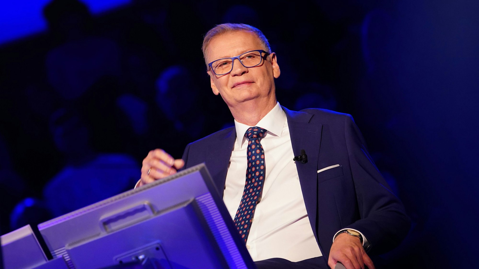 „Wer wird Millionär“-Moderator Günther Jauch sitzt während der Quizshow des Kölner TV-Senders RTL auf seinem Stuhl am Pult uns grinst ins Publikum.